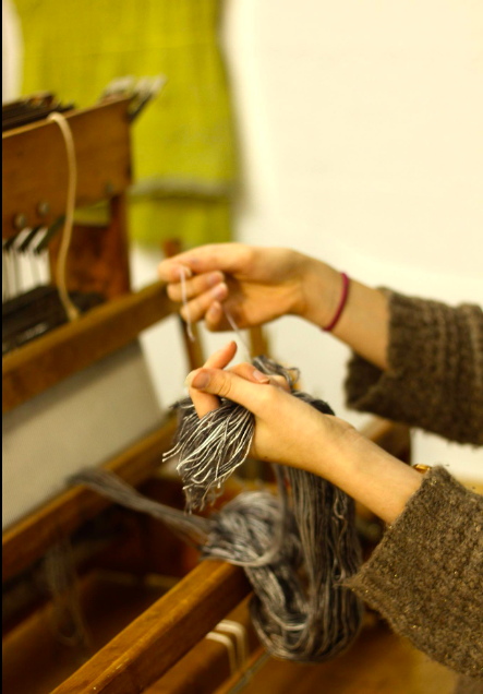 Image of a woman's hands threading a loom. 